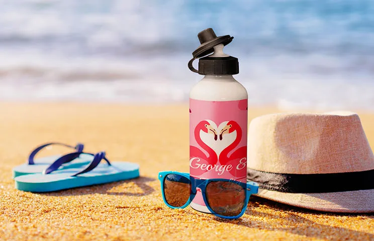 Personalised flamingo water bottle on sandy beach, next to sunglasses & hat. Perfect summer gift!